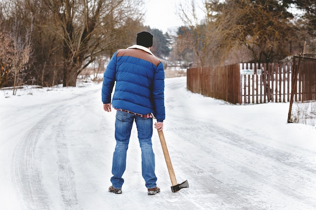 Barbudo loco con un hacha caminando por un camino nevado