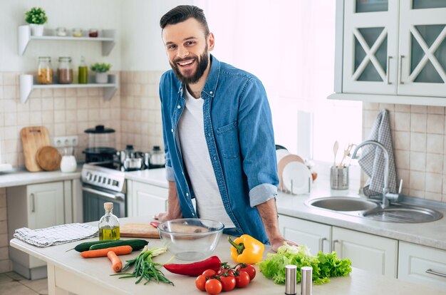 Barbudo sorridente homem bonito na cozinha em casa está posando e