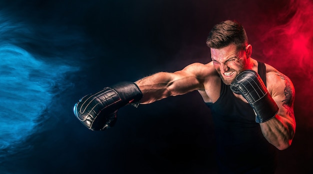 Barbudo tatuado desportista muay thai boxer em camiseta preta e luvas de boxe lutando em um fundo escuro com fumaça. Conceito de esporte.