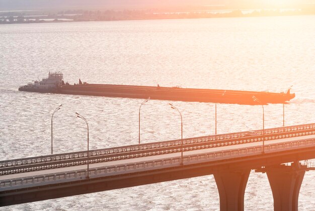 Barcaza y puente de carretera en el río al atardecer o al amanecer.