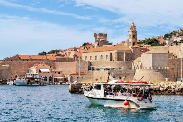 Barco a motor com pessoas no antigo porto no mar Adriático de Dubrovnik, Croácia. Campanário do Mosteiro Dominicano ao fundo