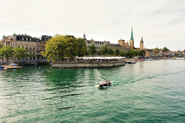 Barco a motor com pessoas no cais do Rio Limmat e Igreja de São Pedro e Igreja Fraumunster no centro da cidade de Zurique, Suíça.