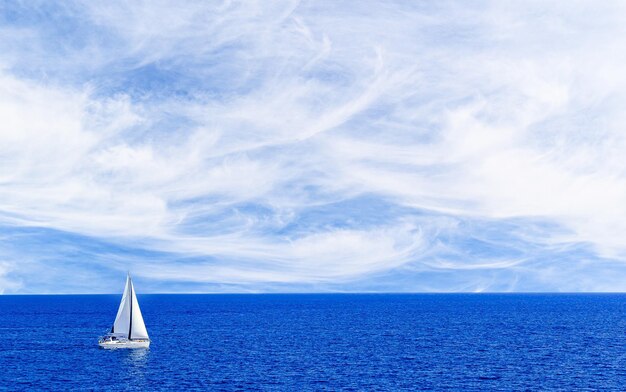 Barco a vela navegando na praia de Maiorca sob um céu azul com nuvens brancas