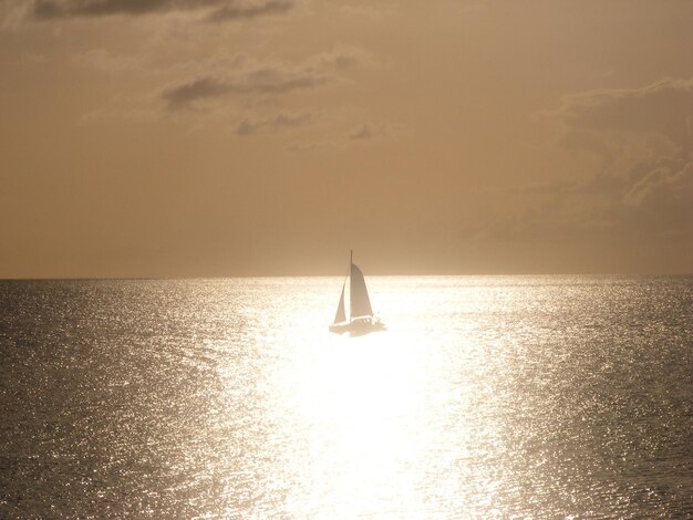 Barco a vela navegando no mar contra o céu durante o pôr-do-sol