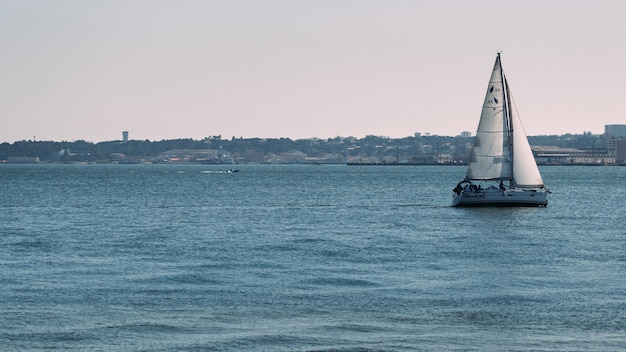 Barco à vela no mar com costa urbana