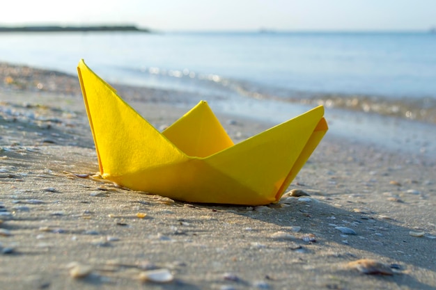 Barco amarelo de papel pequeno na areia perto da água no fundo das ondas do mar