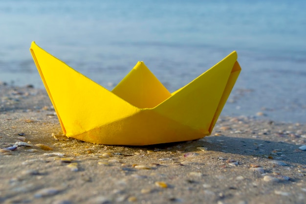 Barco amarelo de papel pequeno na areia perto da água no fundo das ondas do mar