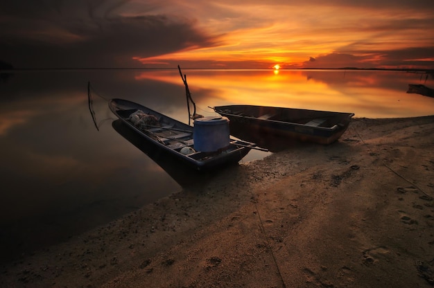 Barco amarrado en la playa contra el cielo durante la puesta de sol