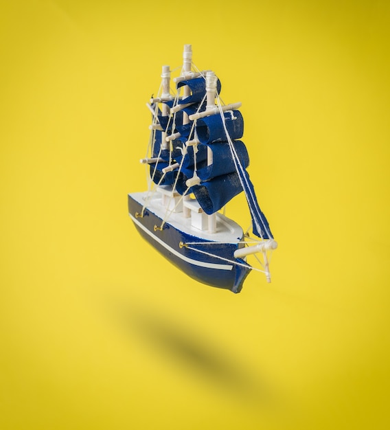 Un barco azul con velas sobre una superficie de color amarillo brillante. Un sueño hecho realidad.