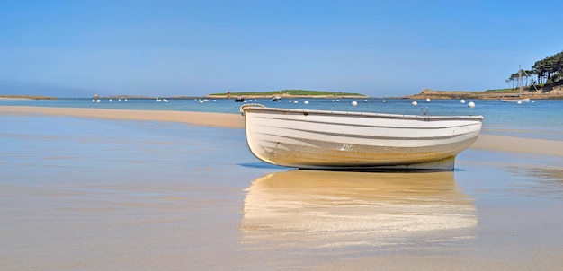 Barco blanco colocado en la arena cerca del mar azul con reflejo en la arena mojada