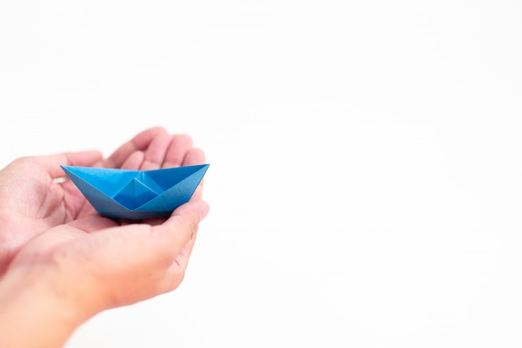 Barco de papel azul que guarda à mão no conceito branco do fundo, da aprendizagem e da educação