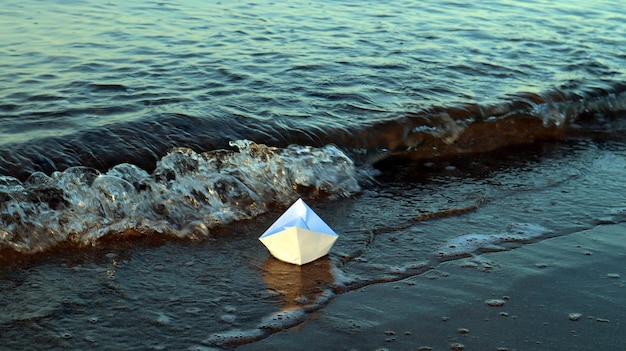 Barco de papel flutua na água azul no mar, símbolo de veleiro de transporte, conceito de viagem, velejar