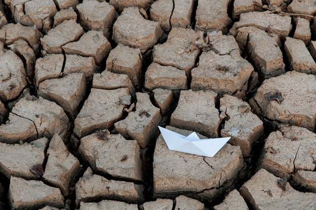 Barco de papel no lago seco, seca conceitual, aquecimento global.