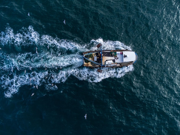 Barco de pesca flutuando na vista aérea do mar azul do drone