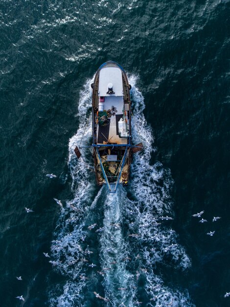 Barco de pesca flutuando na vista aérea do mar azul do drone