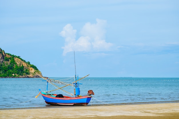 Barco de pesca na praia com céu azul e mar.