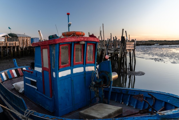 barco de pescadores colorido no cais de palafitas de madeira da Comporta ao pôr do sol em Setúbal, Portugal