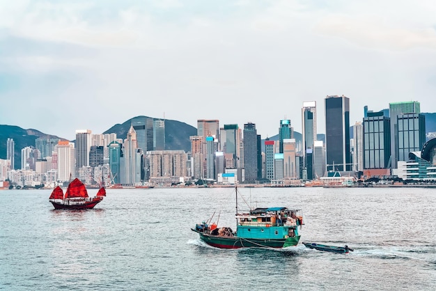 Barco de sucata em Victoria Harbour de HK ao pôr do sol. Vista de Kowloon na ilha de Hong Kong.