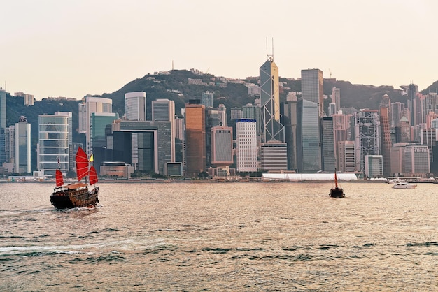 Barco de sucata em Victoria Harbour de Hong Kong ao pôr do sol. Vista de Kowloon na ilha de HK.