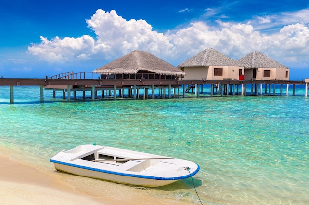 Barco e bangalôs aquáticos em ilha tropical nas Maldivas