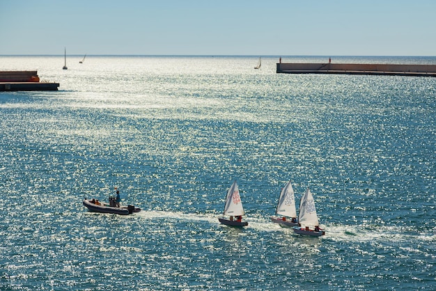 El barco del entrenador acompaña a los veleros de los niños pequeños en la bahía del mar Escuela de yates