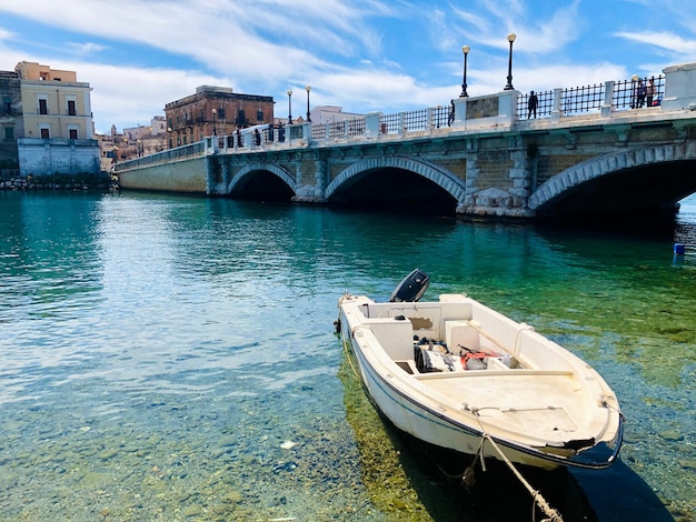 Un barco está atracado en un canal con un puente al fondo.