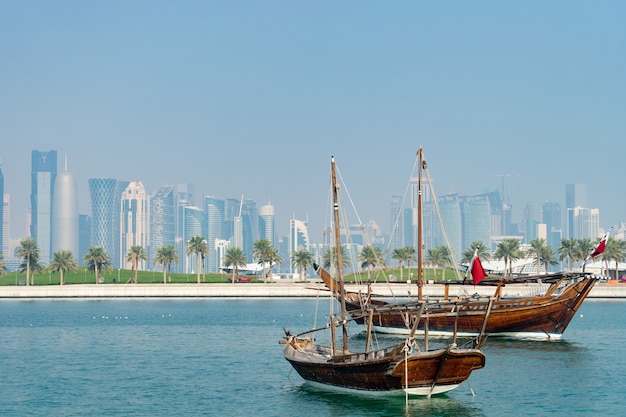 Barco histórico retrô com vista panorâmica turva do horizonte moderno de Doha e palmeiras verdes na superfície