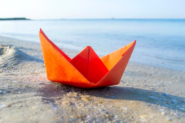 Barco laranja de papel pequeno na areia perto da água no fundo das ondas do mar