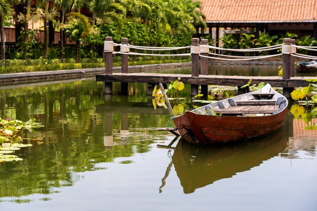 Barco de madera en el estanque cerca del muelle en un jardín tropical en Danang