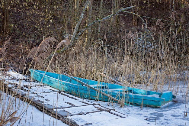 Barco de madera en el lago de invierno. Barco abandonado en el bosque