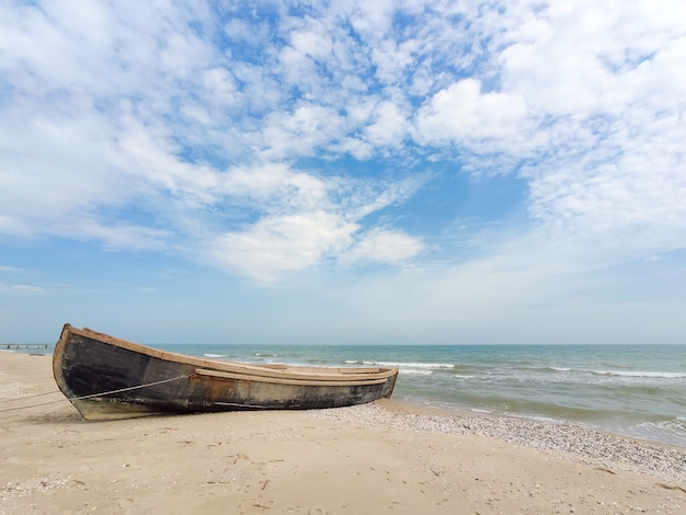 Barco de madera vieja en la orilla del mar, cielo nublado, tiempo soleado.