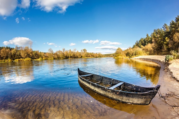 Barco de madera viejo en el banco de un río ancho en día soleado