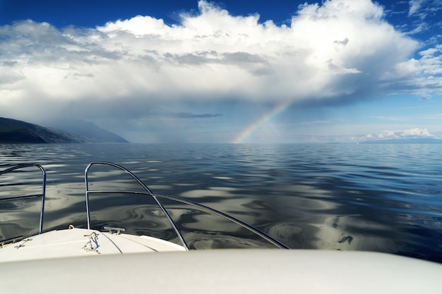 Barco en el mar cerca de la costa nubes blancas y arco iris