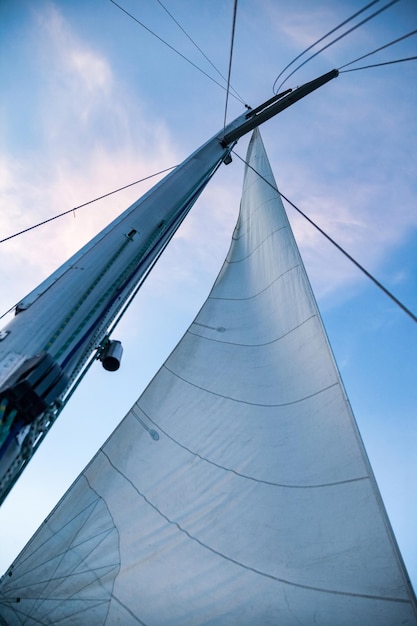 Barco de mástil de vista inferior contra el cielo con nubes cúmulos en el mar Mástil de yate de vela con cuerdas con vela en el fondo del cielo azul