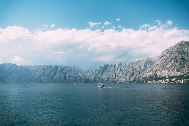 Barco de motor blanco navega a lo largo de la bahía de Kotor contra las montañas