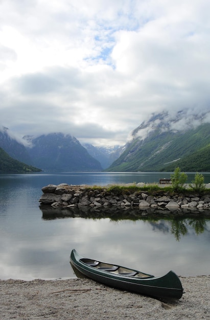 Barco na praia com montanhas e céu nublado ao fundo, Noruega