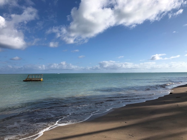 Barco na transparência do céu azul do mar com nuvens e sombras de árvores na areia