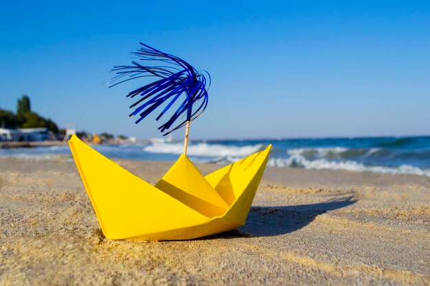 Barco de papel amarillo con decoración de palitos de cóctel en la costa arenosa con mar