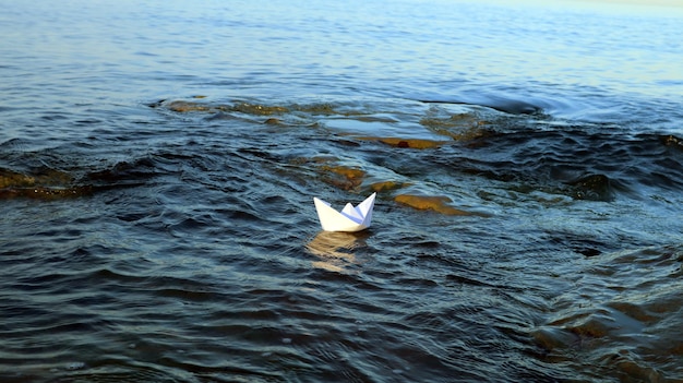 Barco de papel flota en agua azul en el mar, símbolo de velero de envío, concepto de viaje, vela