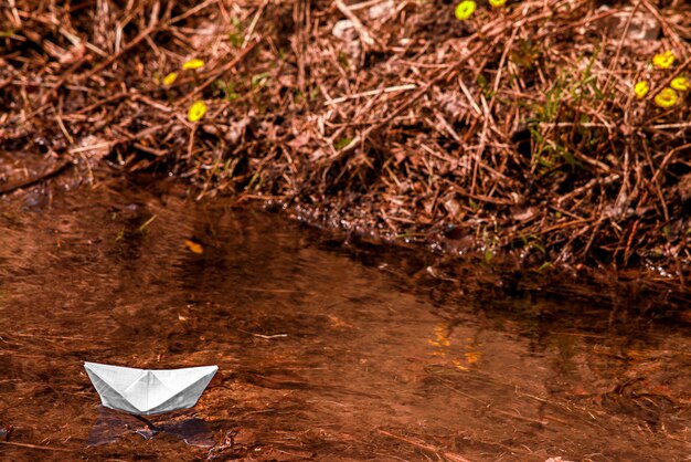 Un barco de papel flota en el río en primavera sobre agua de deshielo contra el fondo del follaje otoñal