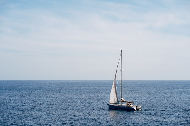 Barco pequeño con una vela blanca ondeando en el viento navega en el mar