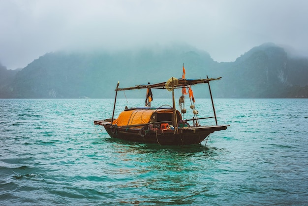 Barco de pesca en la bahía de Ha Long, Vietnam al atardecer. Islas de piedra caliza en el fondo