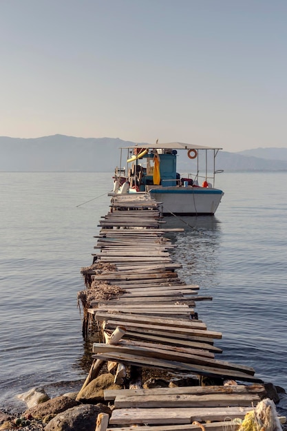 El barco de pesca está amarrado en mar abierto cerca de la orilla y el viejo muelle de madera de cerca de Grecia