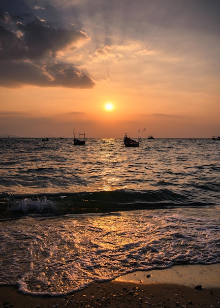 Barco de pesca flotando en la playa de mar tropical al atardecer