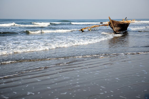 Barco de pesca de madera cerca de la orilla contra el mar azul. Viejo barco con remos en las olas, costa del mar Arábigo, India