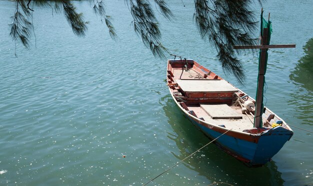 Barco de pesca del pescador anclado en el muelle debajo de un árbol de pino con agua de mar verde azul natural