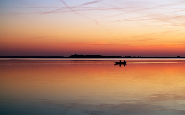 Barco de pesca silueta navegando en el lago al atardecer