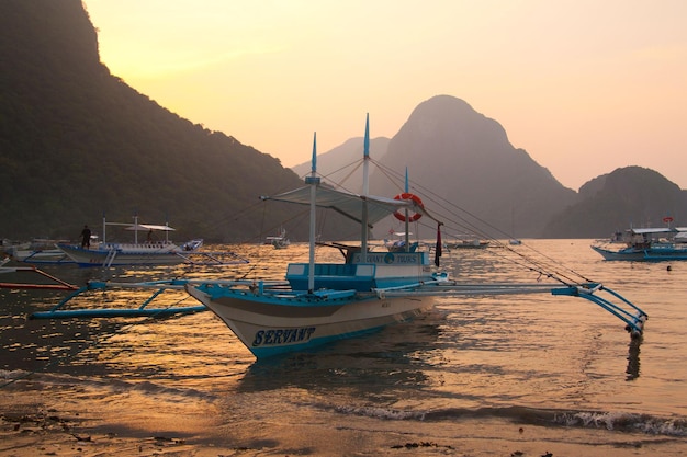 Barco en la playa al atardecer y fondo de montaña en El Nido, Palawan, Filipinas