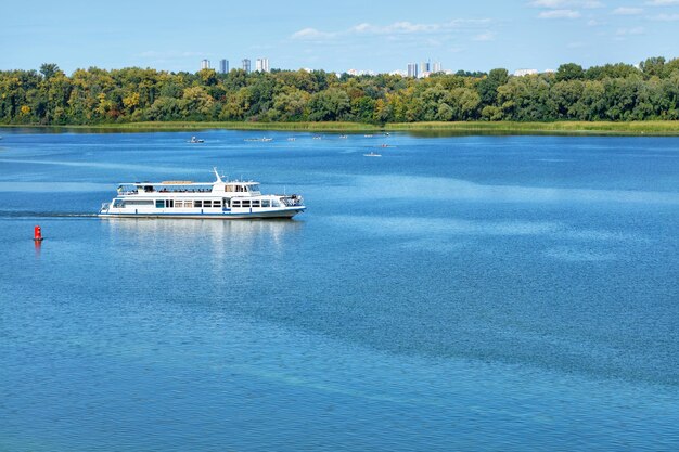 Un barco de recreo va a lo largo de las orillas verdes del dnipro a lo longo de la superficie azul del río durante el día