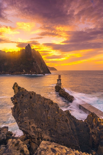 Un barco saliendo en el atardecer naranja del faro de Pasajes San Juan